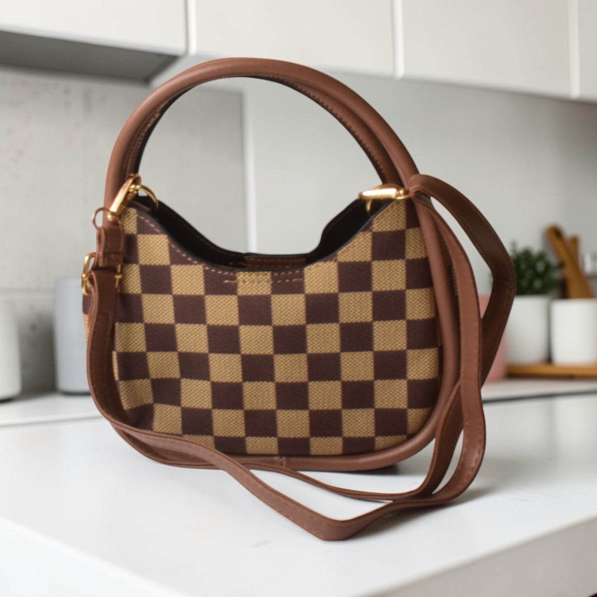 Brown and beige checkered handbag on a white surface with a kitchen background