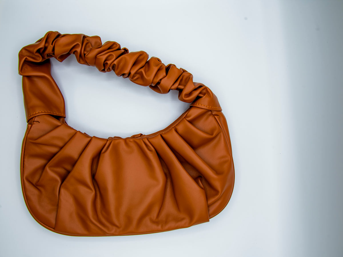 A beige pleated vegan Beige Pleated Everyday Bag vegan leather handbag on plain backgroundleather handbag with a gathered top and smooth surface.