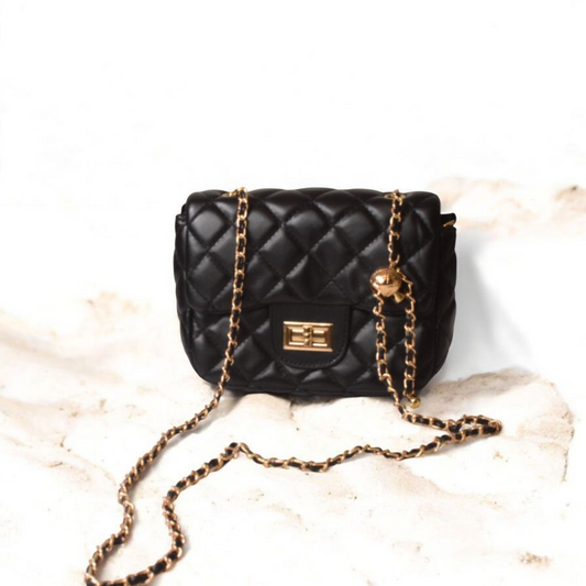 Dorole Cressida Bag in black quilted leather with gold-tone chain strap on a marble surface.