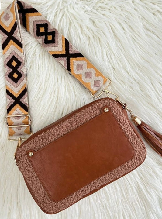 A brown Dorole crossbody purse with a multicolored strap placed on a white furry surface.