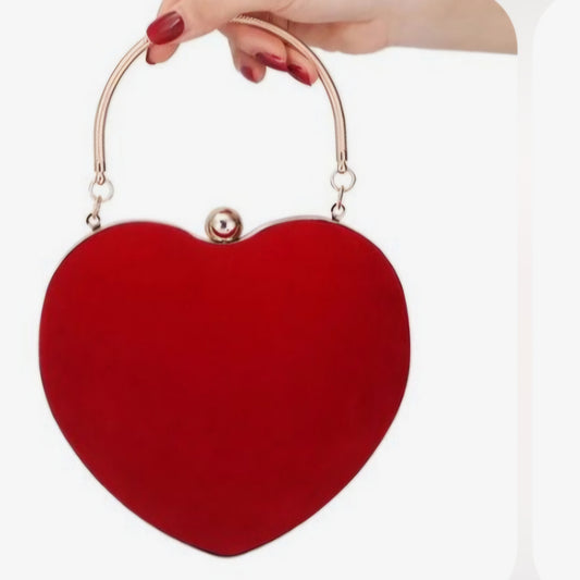 A red heart-shaped clutch with a metallic handle and a strap, held in a person's hand.