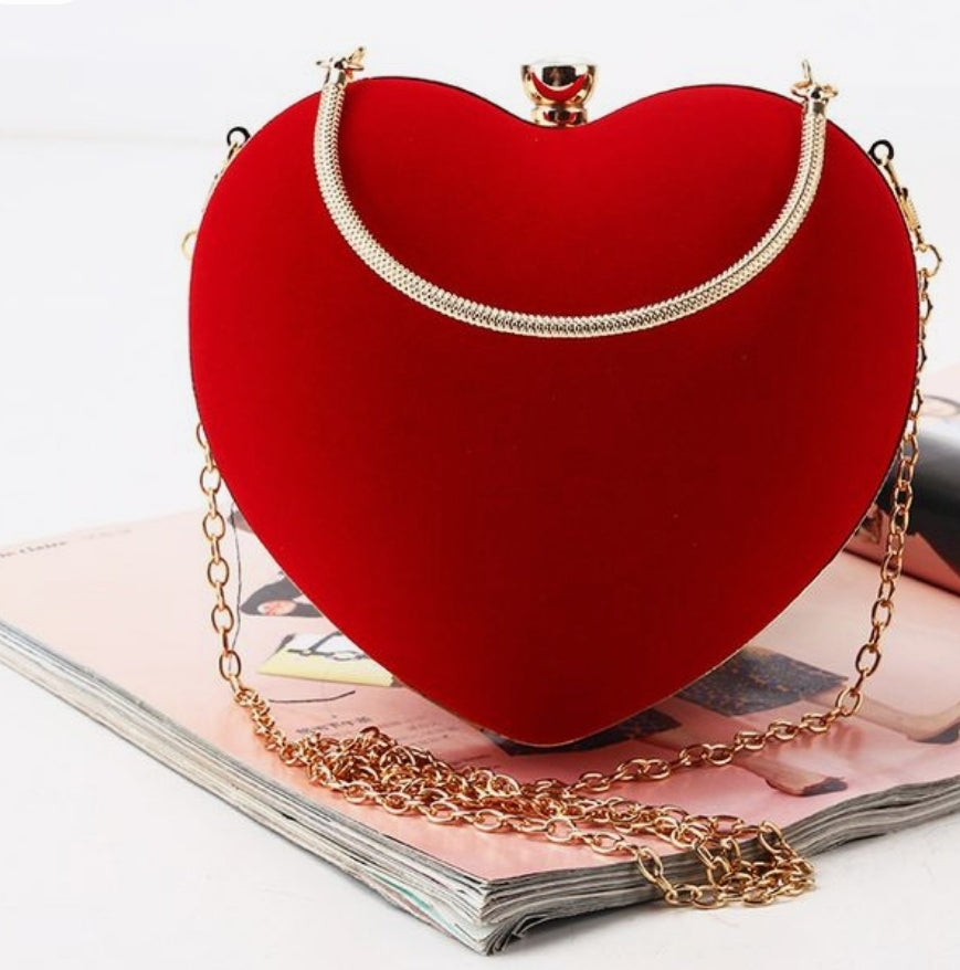 Red heart-shaped handbag with gold chain strap on a magazine