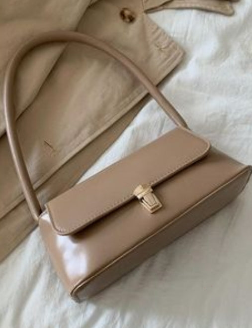 Beige handbag with a gold clasp on a light background