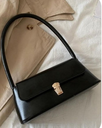 A black Dorole It Girl shoulder bag with a simple design and a metallic clasp, placed on a beige surface.