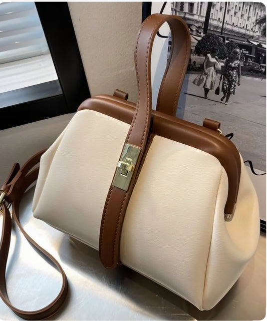 A beige and brown Dorole crossbody bag with a strap and metallic clasp, displayed in front of a blurred background.