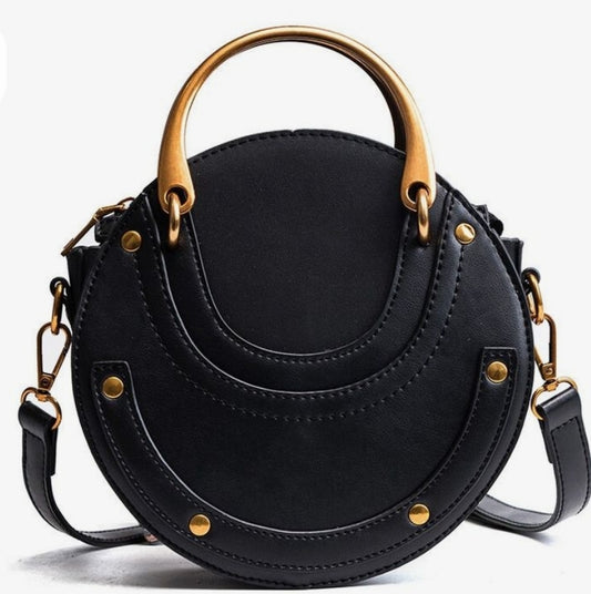 A black round crossbody bag with gold-colored hardware and a shoulder strap.