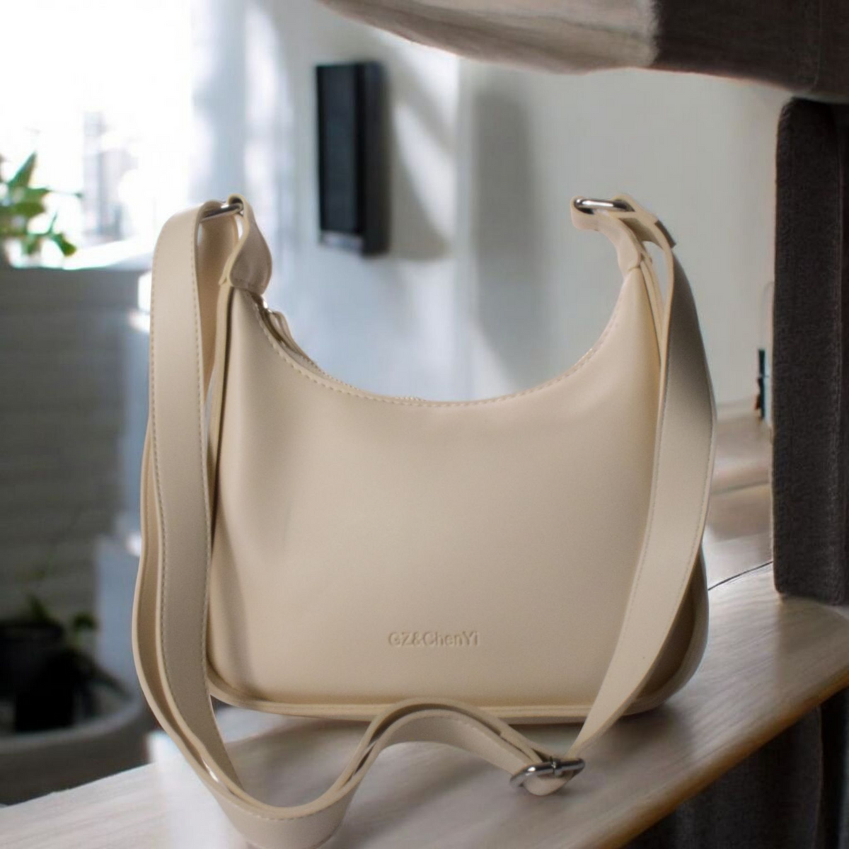 A beige crossbody bag with an adjustable handle, placed on a table.