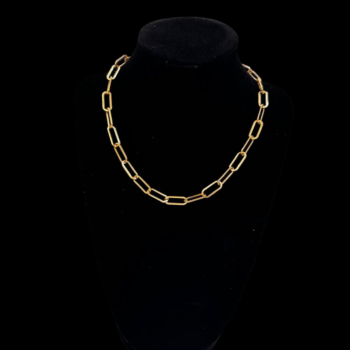 Gold chain necklace on a black velvet stand against a black background