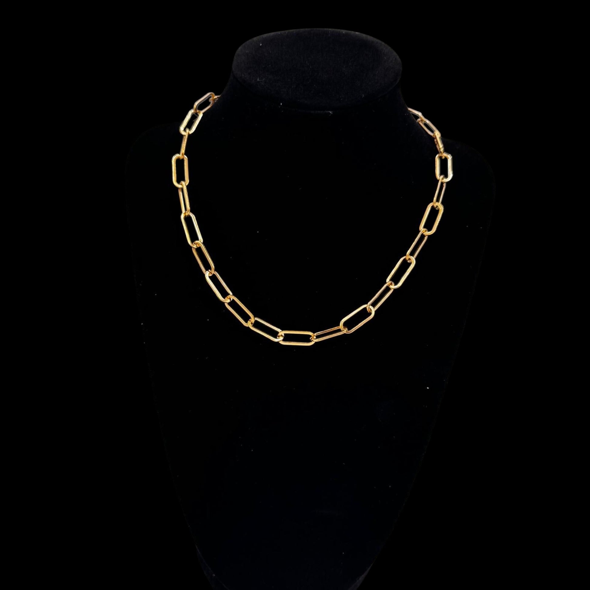 Gold chain necklace on a black velvet stand against a black background