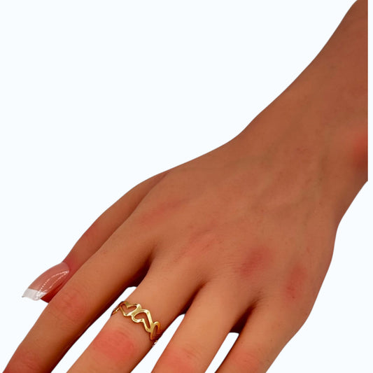 Gold-tone wave band ring featuring interwoven heart patterns worn on a woman's finger.
